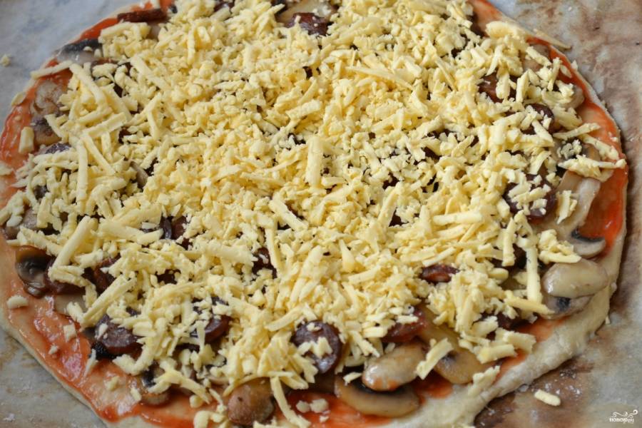 Сверху посыпьте тертым на крупной терке сыром. Отправляйте будущую пиццу в духовку на 40 минут. 
