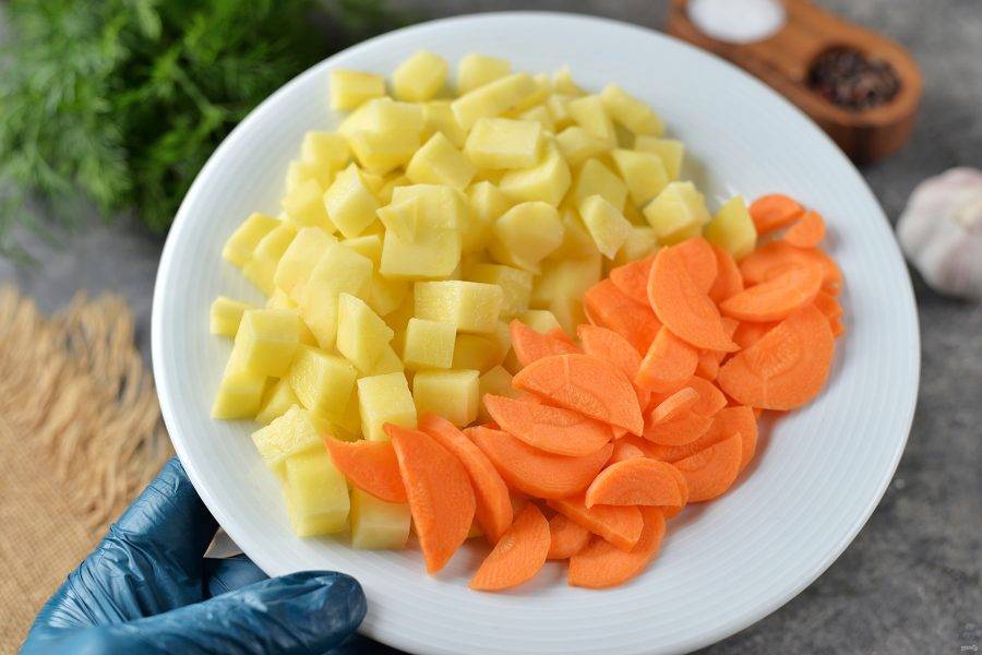 Картофель нарежьте кубиком, морковь — тонкими ломтиками, добавьте в кастрюлю, варите еще 15 минут.