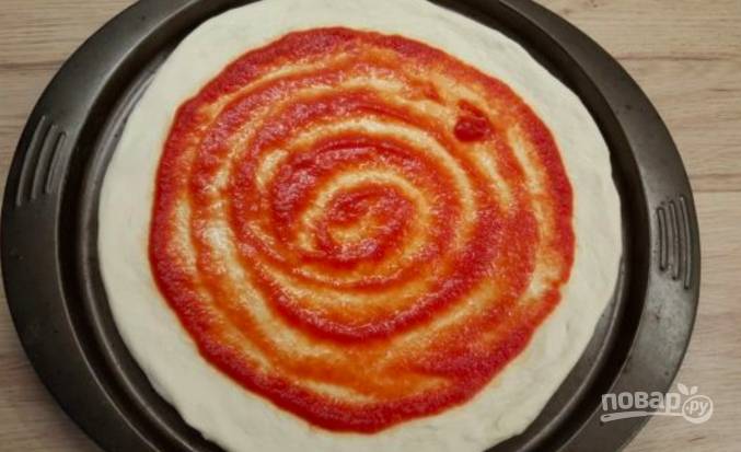 Первым делом раскатайте тесто на присыпанной мукой поверхности и сформируйте круг. Перенесите основу на противень или в форму для выпечки. Нанесите на тесто томатную пасту. Духовку разогрейте до 220 градусов.