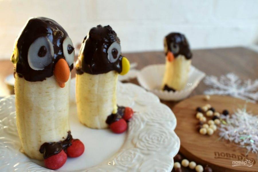 Поставьте конфеты  M&M's на места клюва и ног пингвинов. На лепестки миндаля нанесите по  капельке шоколада - это будут глаза пингвинов. Подавайте сразу, чтобы банан не успел потемнеть.