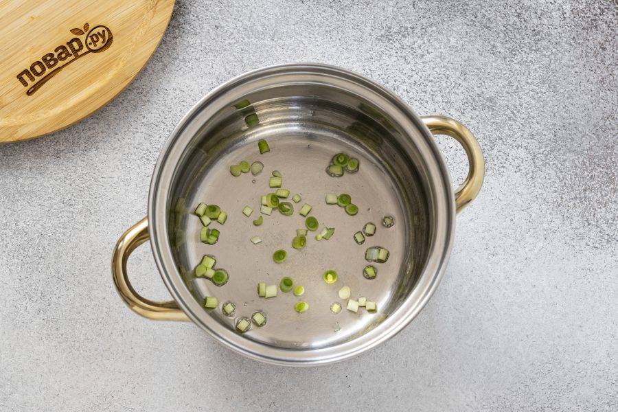 Зеленый лук мелко порежьте. Разогрейте растительное масло в кастрюле. Немного обжарьте белую часть зеленого лука.