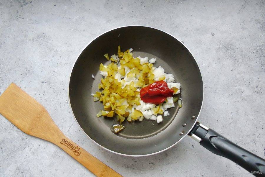 Лук и соленый огурец мелко нарежьте. Выложите в сковороду, добавьте томатную пасту.