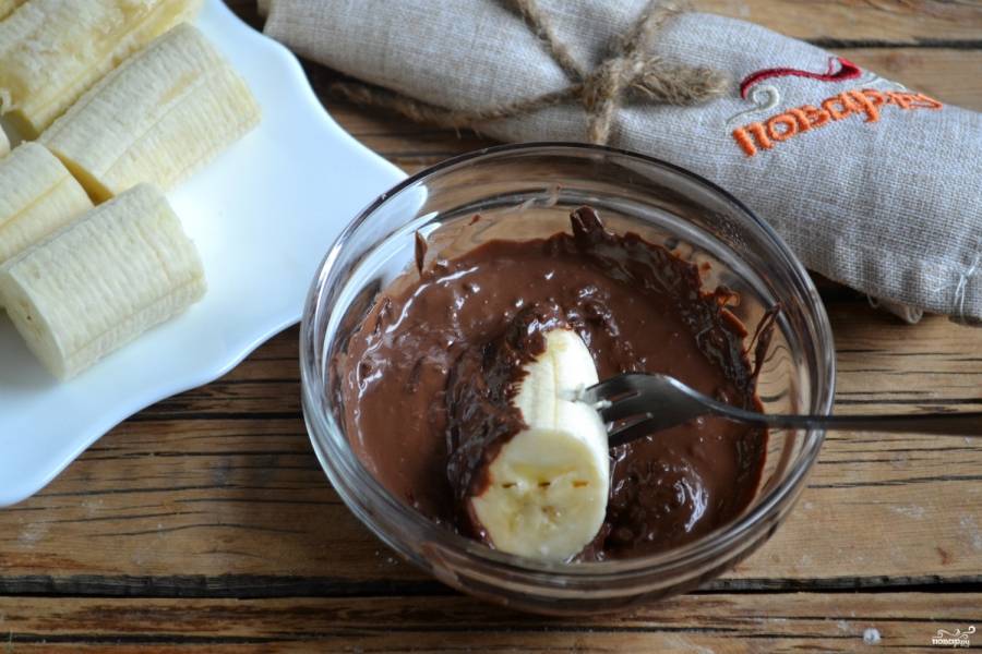 Каждый кусочек банана обмакните в шоколад и поставьте на тарелку стороной без шоколада.
