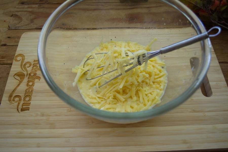 В отдельной миске взбейте яйца с молоком. Добавьте соль и специи. Залейте полученной массой нашу начинку. Натрите твердый сыр и добавьте в заливку.
