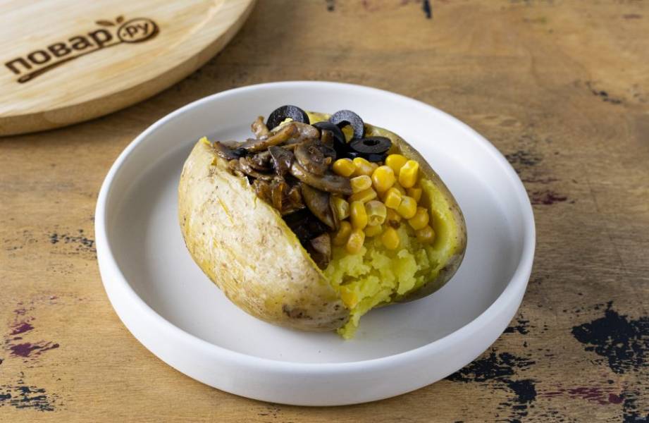 Выложите начинку в картофель жареный лук с грибами, кукурузу и нарезанные маслины. Сверху посыпьте свежей зеленью и полейте майонезом.