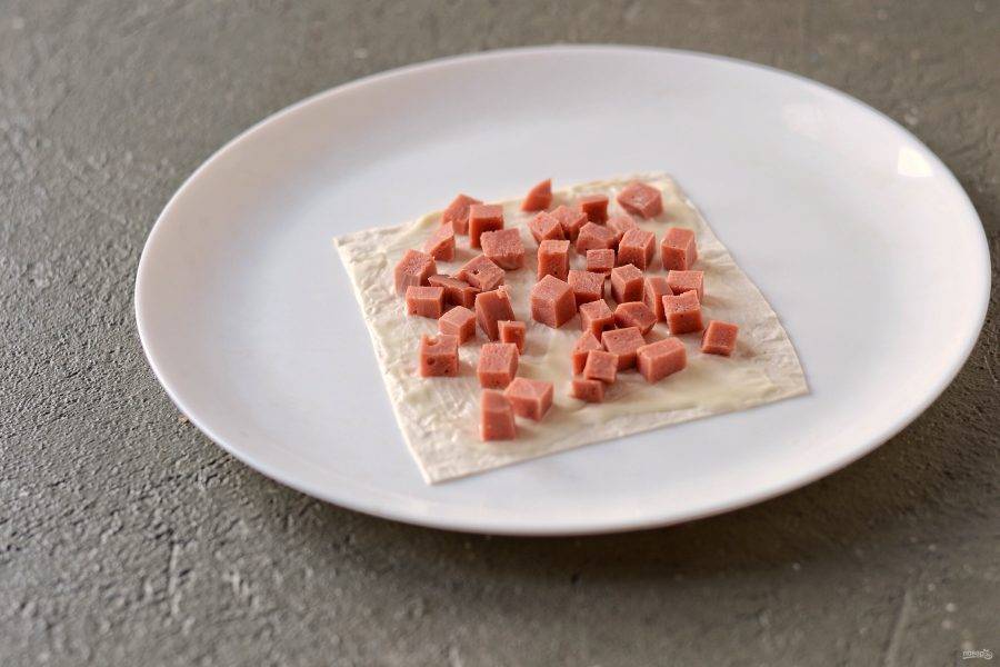 Смажьте один квадратик лаваша майонезом, затем выложите ровным слоем колбасу. 
