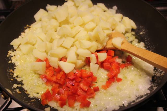 Растопите сливочное масло на сковороде. Обжарьте на нем мелко нарезанный лук. Добавьте нарезанный болгарский перец и картошку. Обжаривайте вместе несколько минут.