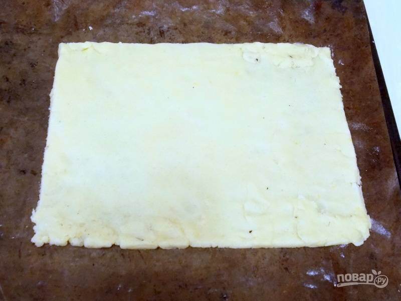 Достаньте тесто и разделите его на 2 части. Уберите одну часть в холодильник, а другую раскатайте на столе с мукой в прямоугольник 30 на 35 см. Переложите на противень, застеленный бумагой для выпечки. 