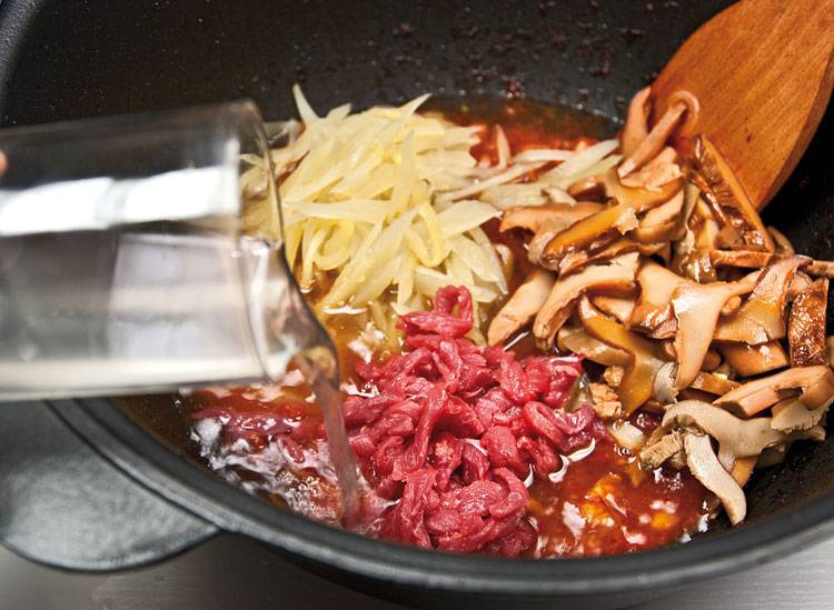 Теперь можете положить соленые огурцы, грибы и оставшуюся часть нарезанной говядины. Тут же залейте содержимое сковороды стаканом огуречного рассола. 