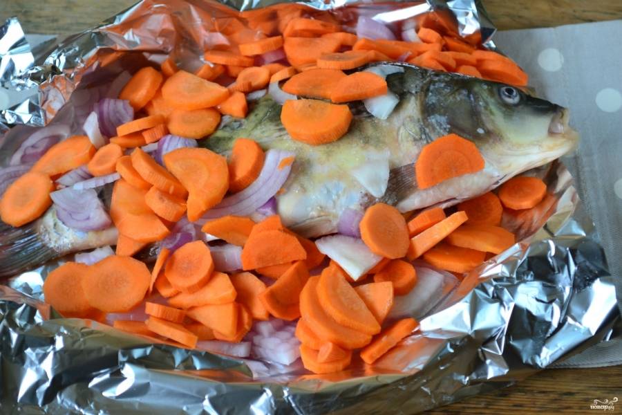 Положите рыбку в противень, застеленный фольгой, сверху выложите овощи, посолите. По желанию предварительно можно слегка присыпать солью рыбу внутри.