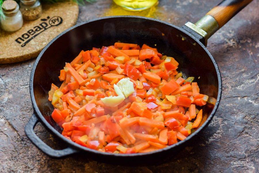 В сковороде прогрейте немного растительного масла, выложите лук, морковь, перец. Жарьте на умеренном огне 5-7 минут. Добавьте раздавленный зубчик чеснока в сковороду.