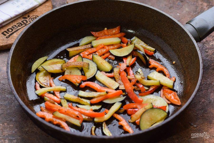 В сковороде разогрейте растительное масло и выложите перец и баклажан. Жарьте овощи 7-8 минут.