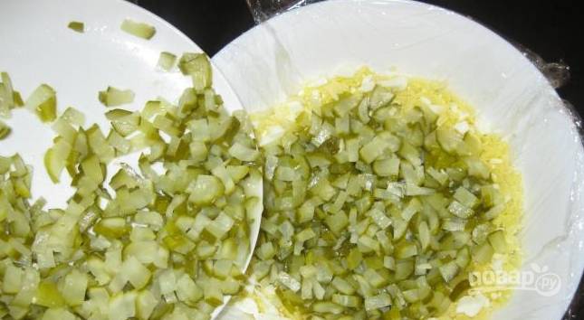 2. Дальше важно застелить глубокую миску полиэтиленовой пленкой, салат мы будет потом переворачивать. Сначала выкладываем сырно-яичный слой, затем промажем его сметаной. Потом — горошек и огурчики. 