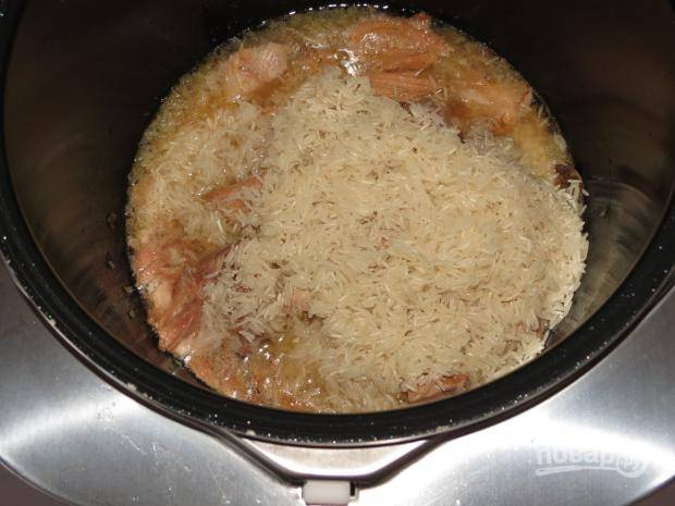 На готовый лук выложите тушёнку и промытый рис.