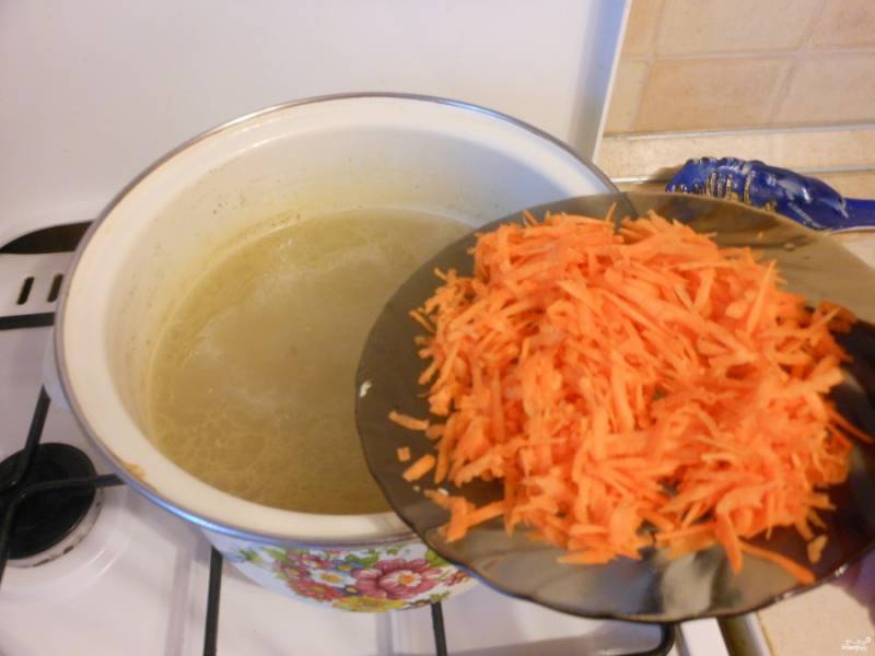 Поставьте бульон на огонь, дайте ему закипеть.
Тем временем натрите морковку на крупной терке.
Бросьте в кипящий бульон морковку.