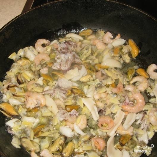 На горячую сковородку налейте немного растительного масла и выложите морепродукты. Обжарьте их до полуготовности и уберите в сторону.