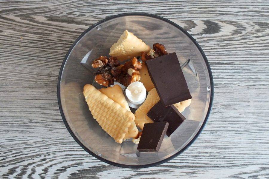 В чаше блендера измельчите в среднюю крупку печенье, половину количества шоколада и орехи.