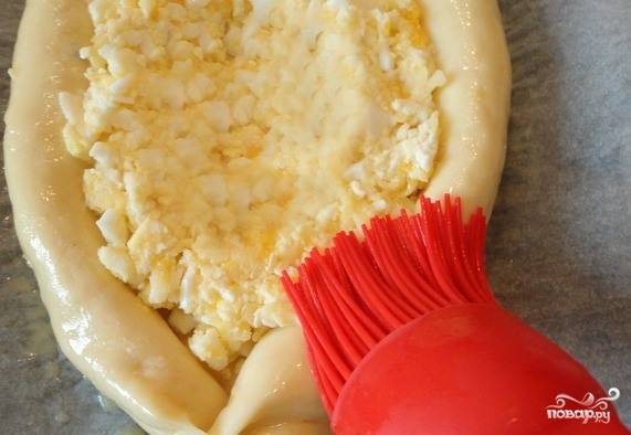 Выложите в хачапури начинку из сыра и яиц. Сделайте в ней небольшое углубление, в которое потом вы будете вбивать сырое яичко. В отдельной посуде взбейте желток с молоком или водой, макайте в смесь кисточку и обмажьте хачапури со всех сторон. Нагрейте духовку до двухсот двадцати градусов, выложите хачапури на противень и запекайте пятнадцать минут.