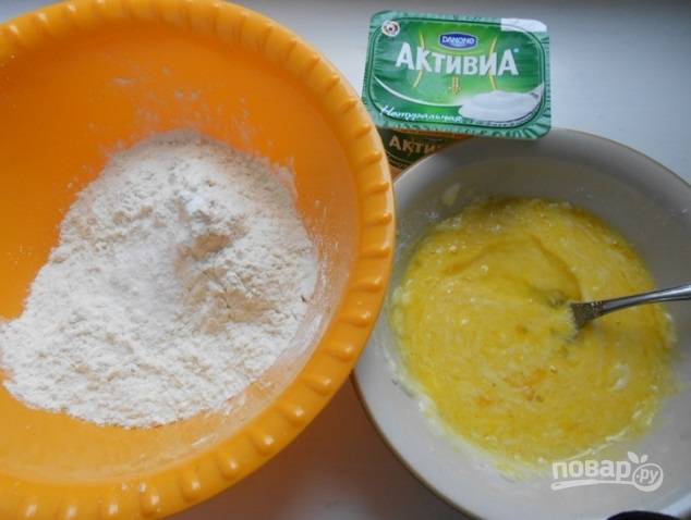 В другой миске перемешайте соду с мукой и солью. К яичной массе всыпьте половину мучной и часть йогурта. Перемешайте. Затем добавьте оставшиеся части. Замешайте тесто.