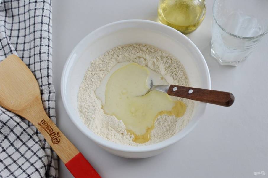 Влейте кефир и растительное масло, начните ложкой замешивать тесто. Если нужно добавьте немного муки.