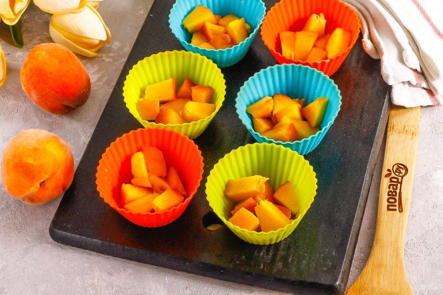Промойте персики в воде и разрежьте пополам каждый плод, удалите косточки. Нарежьте мякоть кубиками и выложите в силиконовые корзинки или другие формочки для приготовления суфле.