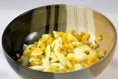 3. Кукурузу откиньте из банки на дуршлаг, затем выложите в миску к нарезанным яйцам.