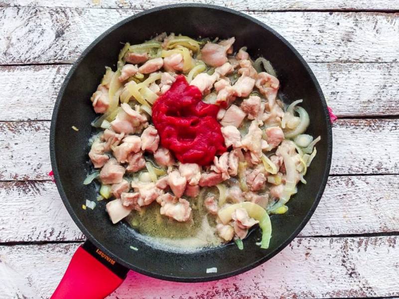 К жареной курице с луком добавьте томатную пасту, хорошо перемешайте и тушите 3-4 минуты. 