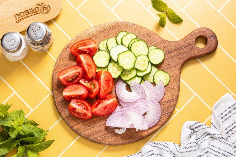 Огурцы нарежьте кружочками. Помидоры нарежьте дольками, а красный лук полукольцами.