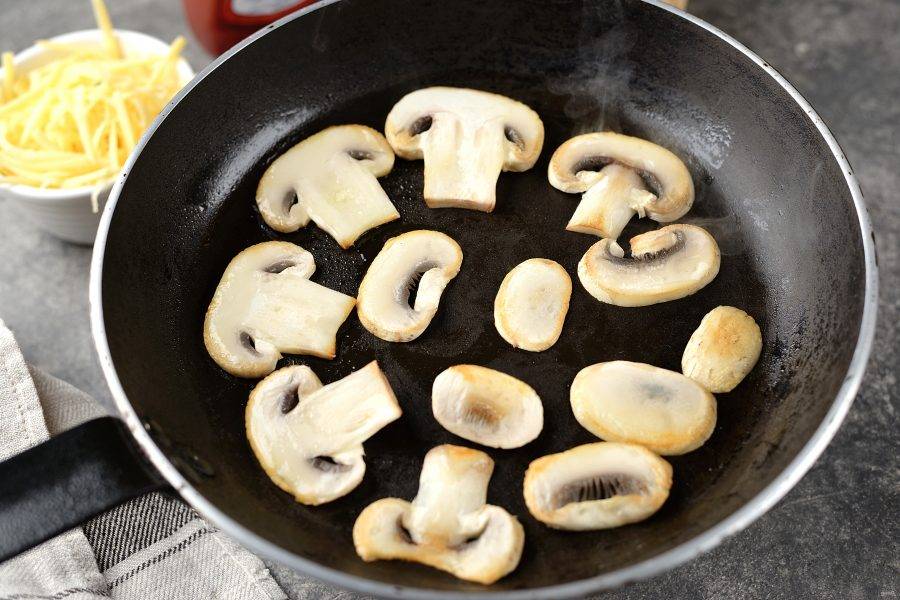 Разогрейте в сковороде немного растительного масла, грибы нарежьте тонкими ломтиками, обжарьте их до слегка румяной корочки с обеих сторон.  