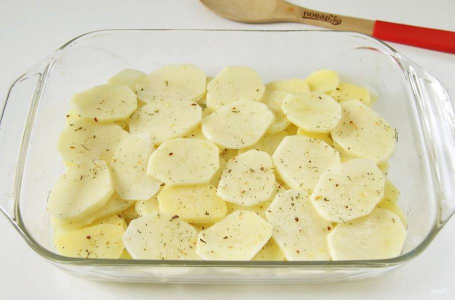 Форму для запекания смажьте маслом и выложите равномерно нарезанный кружочками картофель. Посолите и присыпьте картофель специями.