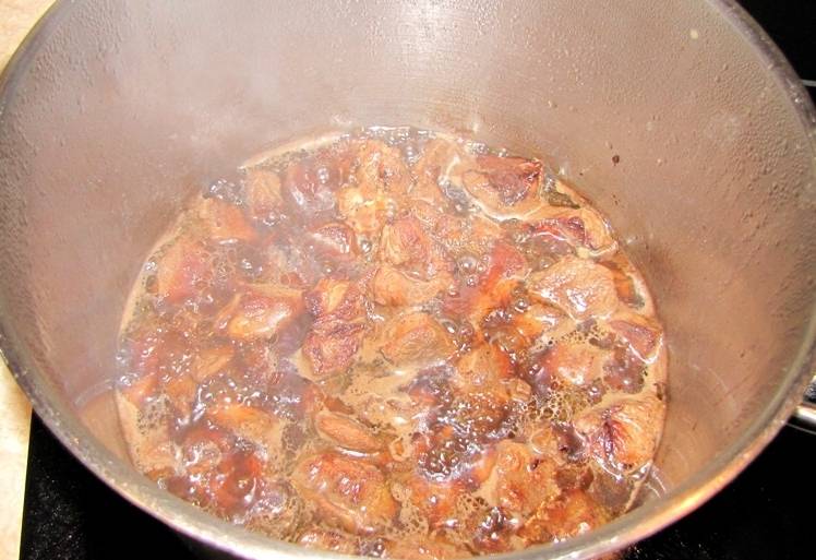 Перекладываем обжаренное мясо в кастрюлю, а на сковороду наливаем пол стакана кипятка и при помощи деревянной лопатки растворяем в воде все оставшиеся после обжарки соки и так далее. Эту смесь переливаем в кастрюлю и добавляем в нее кипяток, всего жидкости должно быть около 1 литра. Тушим баранину в течение 15-20 минут на медленном огне.