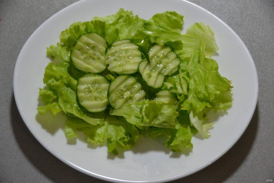 Выложите огурец поверх салатных листьев.