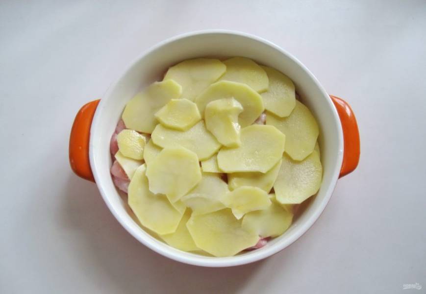 Картофель очистите, помойте, нарежьте пластинами. Выложите в форму на куриное филе, немного посолите.