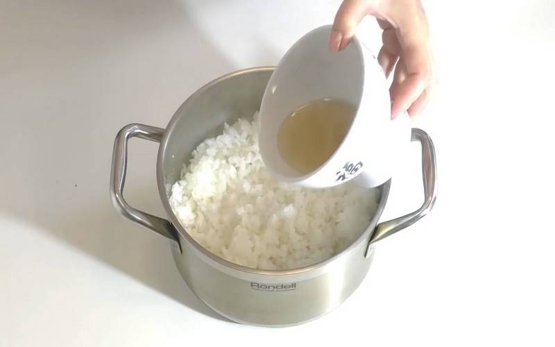 Готовый рис выложите в посуду побольше, слегка разрыхлите легкими движениями при помощи деревянной лопатки, влейте заправку и аккуратно перемешайте рис.