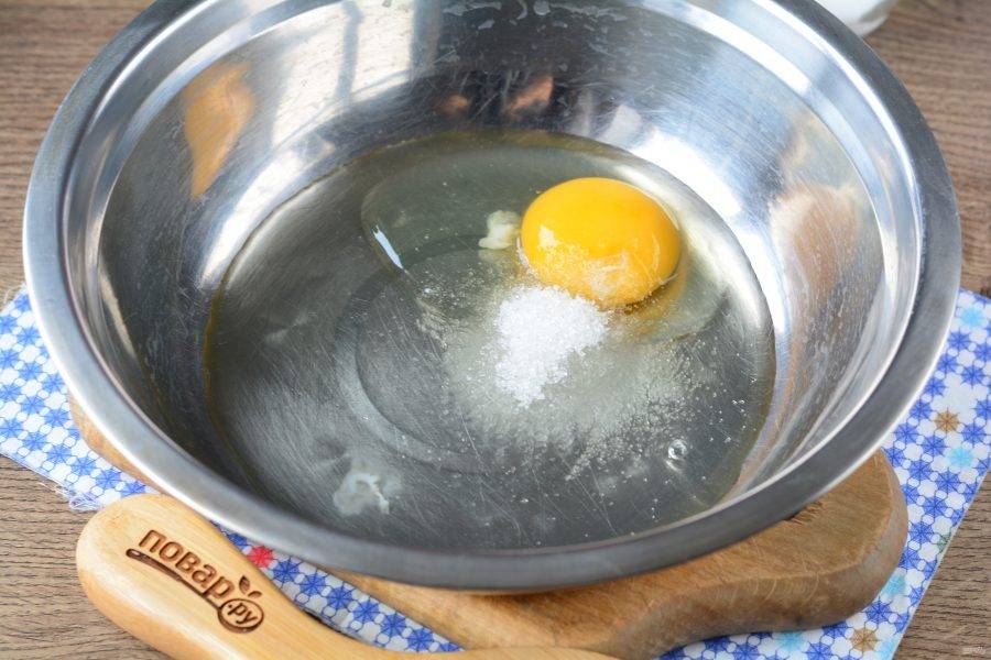 Приготовьте блинное тесто. Вбейте 1 куриное яйцо в миску, всыпьте сахар и соль.