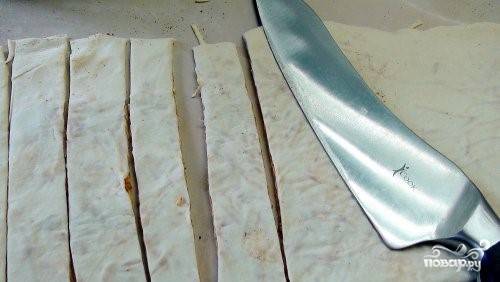 3. Тесто с начинкой сложите пополам. Возьмите скалку, слегка раскатайте сложенный пласт. Затем ножом с острым лезвием нарежьте тонкие полоски (1,5 см).