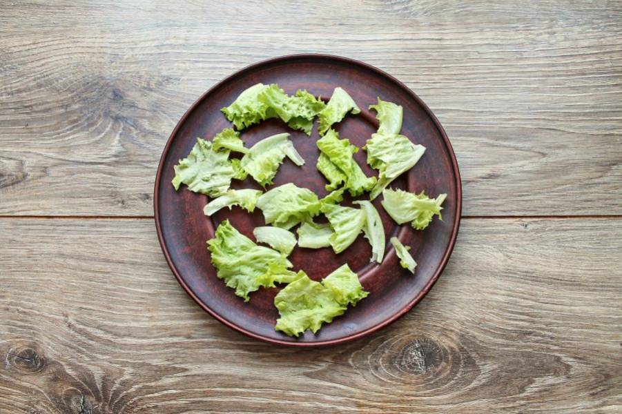 Листья салата порвите руками и выложите на дно сервировочной тарелки.