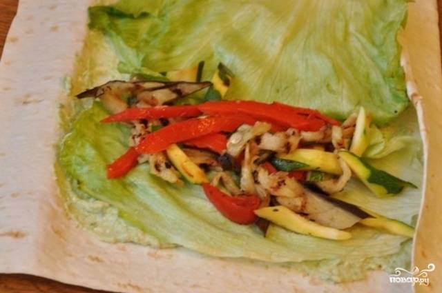 Сверху на крем выложите листья салата и подготовленную овощную начинку, затем аккуратно сверните лаваш.
Перед подачей рулет можно слегка поджарить на сковороде. Но это опционально