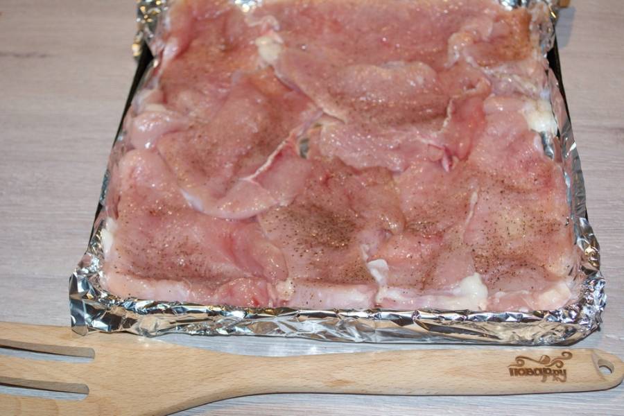 Подготовленное мясо укладываем на противень. Я предпочитаю максимально уменьшить количество грязной посуды. Поэтому застилаю противень фольгой, сложенной вдвое. Так удобнее, и мыть ничего не приходится. На подготовленный противень выложите отбитые кусочки куриного филе.