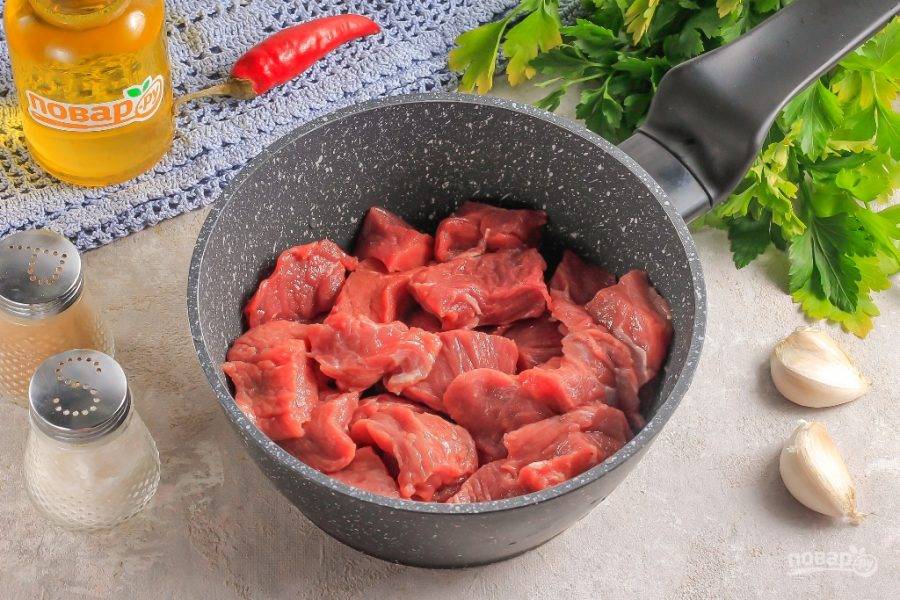 Влейте в казан или сотейник растительное масло. Нарежьте говядину порционными кубиками. Чем мельче нарезка, тем быстрее она приготовится. Добавьте нарезку мяса в емкость к маслу.