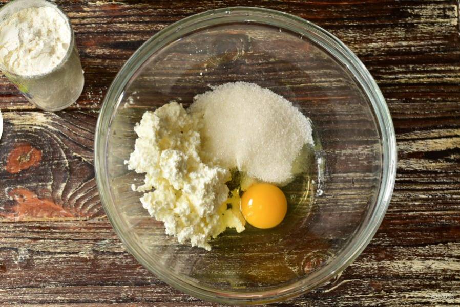 В миску вбейте яйцо, выложите творог и всыпьте сахар.