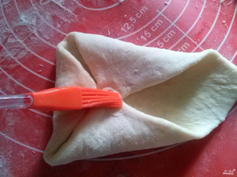 Запечатанные хачапури раскатайте скалкой в квадрат, сыр при этом впечатывается в тесто. Защипните края в середину хачапури, смазывая каждый уголок белком.