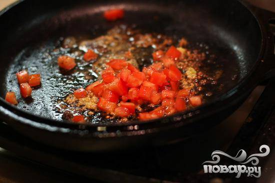 3. Уменьшить огонь до минимума. Мелко нарезать чеснок и петрушку. Нарезать помидор. Добавить в сковороду сливочное масло и чеснок. Жарить 10 секунд, а затем добавить помидоры.