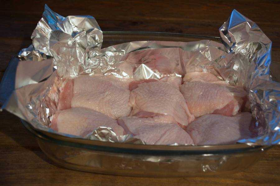Куриное мясо вымыть. Не обязательно брать окорочка. Можно взять всю курицу целиком, нарезать на порционные куски и уложить в форму.
Форму застелить фольгой. Кусочки курицы хорошо посолить и уложить в форму для запекания плотно.