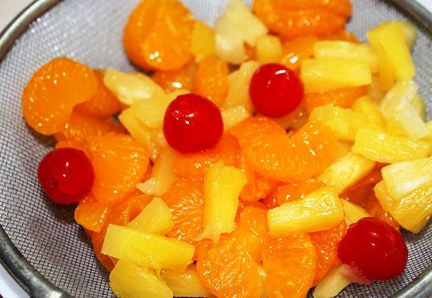 Разберите мандарины на дольки, очистите их от волокон. Промойте вишни и удалите косточки, порежьте консервированные ананасы.