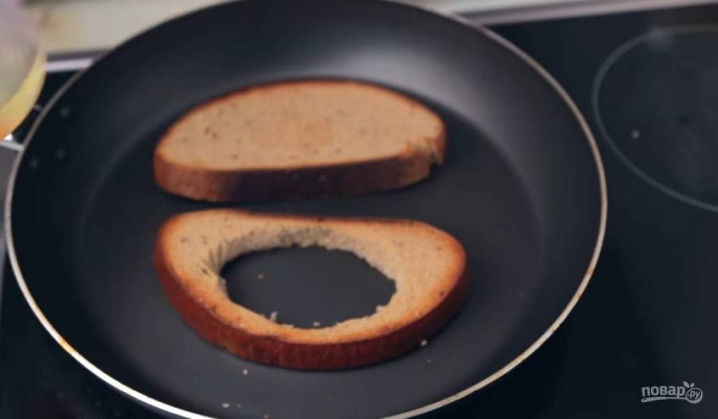 2. Хлеб нарежьте на ломтики толщиной 1 см. В одном ломтике вырежьте круг для яичницы. Обжарьте хлеб на сухой сковороде на небольшом огне до золотистой хрустящей корочки. 