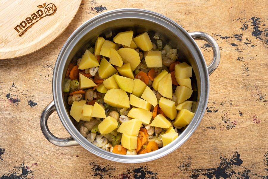 Переложите овощи и грибы в кастрюлю. Добавьте очищенный и нарезанный кубиками картофель.