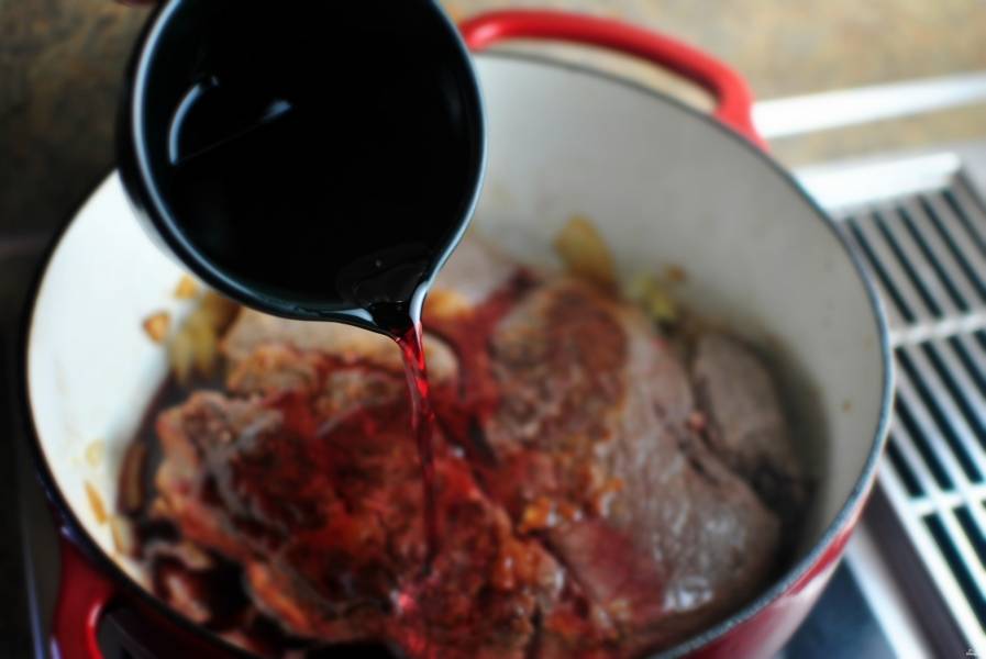 Затем верните мясо к обжаренному луку с чесноком. Влейте вино.