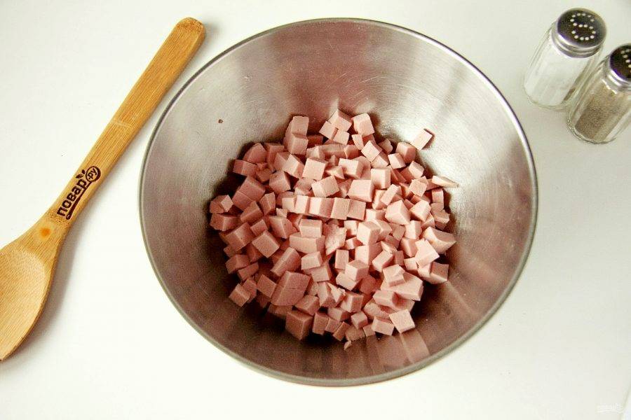 Колбасу нарежьте небольшими кубиками и сложите в глубокую миску или салатник.