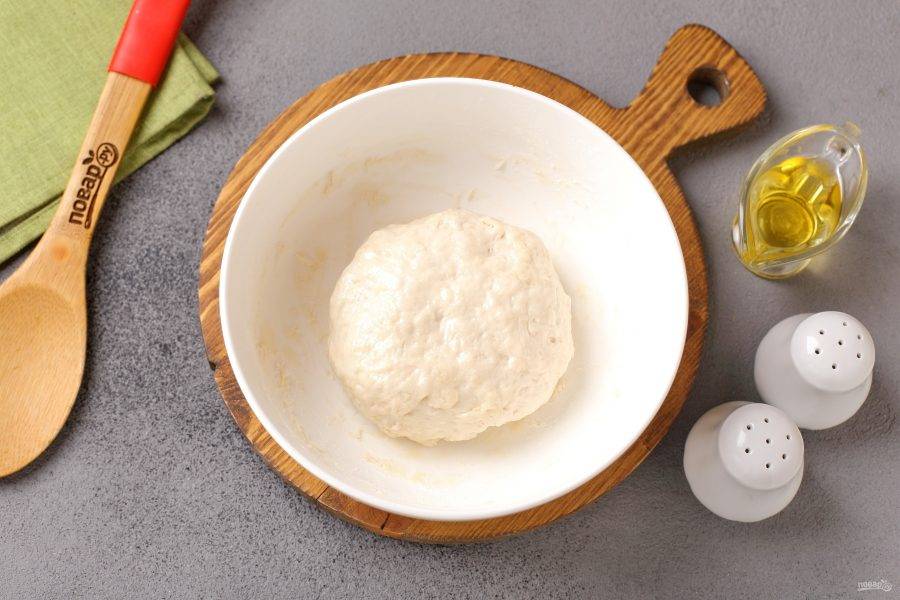 Замесите руками мягкое, чуть липкое тесто. Смажьте его маслом, соберите в шар, накройте миску пищевой плёнкой и оставьте в тёплом месте примерно на час.